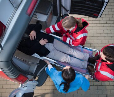 top view of paramedic team moving man on ambulance stretcher into car
